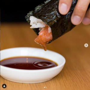 Guest dipping KazuNori sushi hand roll into soy sauce